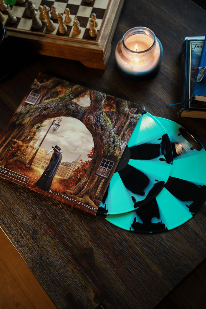 A The Dear Hunter Act IV limited edition mint green & black cornetto splatter vinyl with an illustrated cover sits on a wooden table next to a lit candle, chessboard, and book.