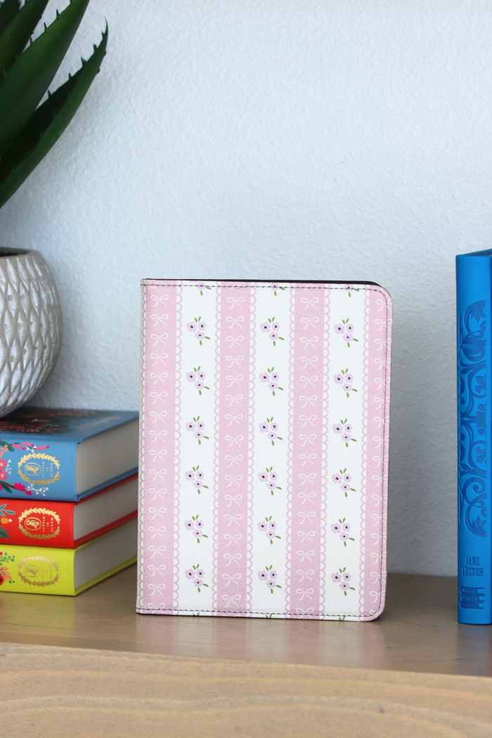 Pink floral striped kindle on a wooden surface with books and a plant in the background