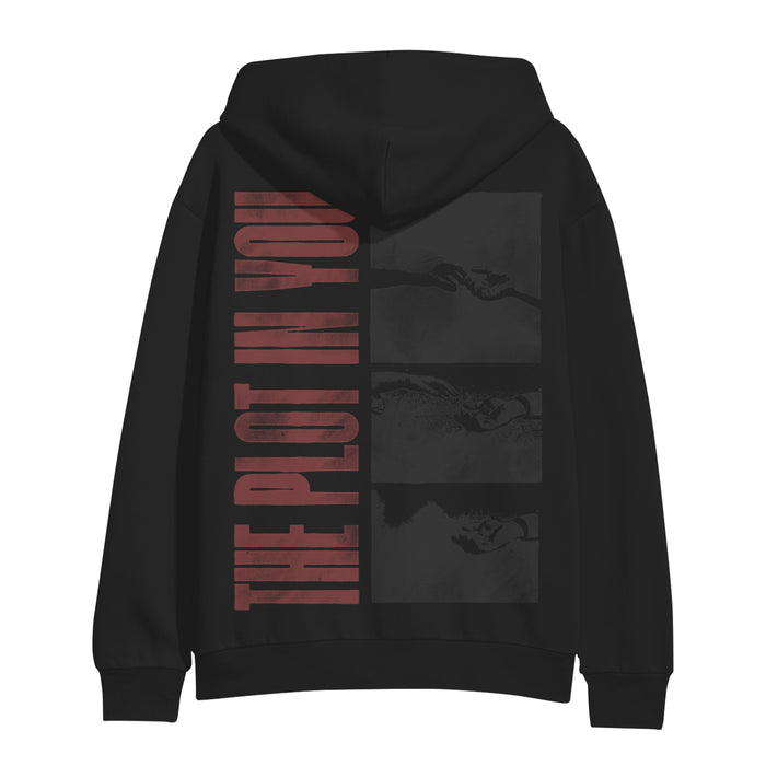 A black hoodie by The Plot In You, featuring bold red lettering down the back and three grayscale panels of hands reaching for each other.