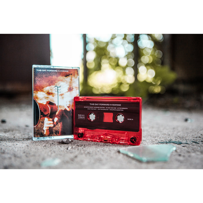The cassette is pictured on cement, with broken glass in front of it. The tape is a transparent red.