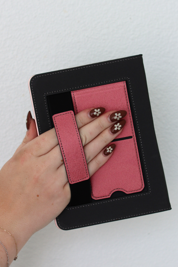 Hand holding a black kindle with a pink interior against a white background