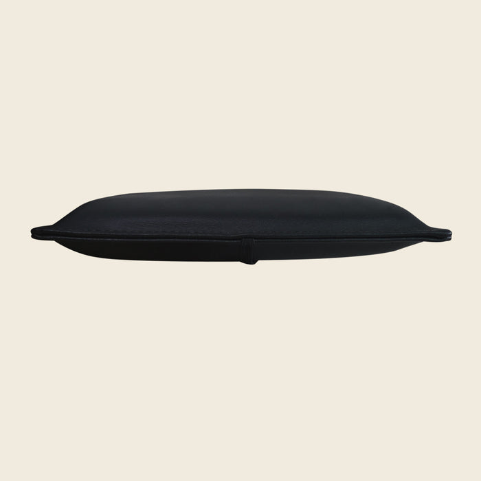 Black upholstered Pilates pillow for Reformer shoulder blocks, shown from a low side angle.