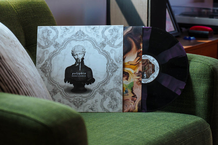 A Polyphia Renaissance Limited Edition Black and Purple Cornetto vinyl record, partly slid from its ornate cover depicting a veiled statue, rests on a green armchair in a cozy living room.