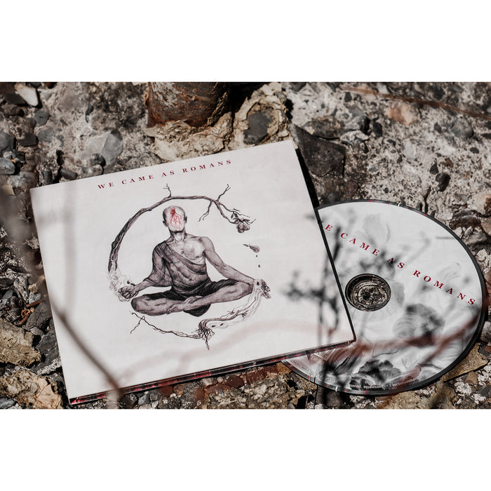 Square CD with a faceless person in a robe sitting with their legs crossed. Around them is a tree branch sprouting from one of their hands. Above the artwork, there is red text that says WE CAME AS ROMANS. Next to the cover is a white CD disc that says WE CAME AS ROMANS in red. They are both laying on top of leaves and rocks.