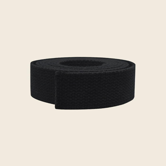 Black woven cotton webbing belly strap for Pilates Cadillac, coiled on a beige background.