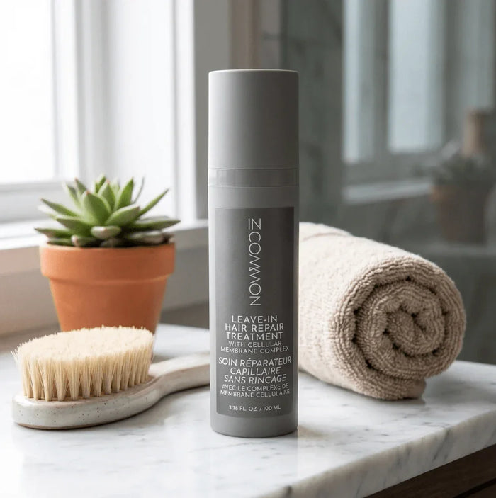 Leave-in hair repair treatment bottle with brush, towel, and potted plant on a bathroom counter