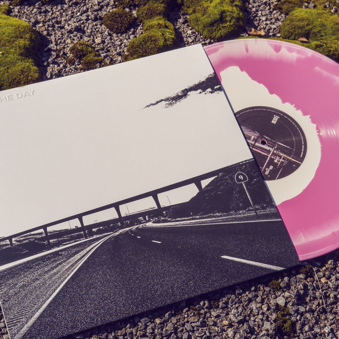Square Vinyl, black and white coloring. Highway leading to an overpass with a sign reading "9" on the right hand side. Vinyl disc on the right hand side, pink and white coloring. Both items on top of small rocks and moss.