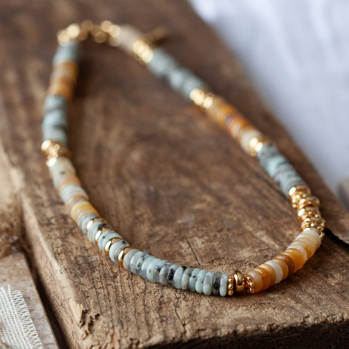 Close-up of beaded gold-tone necklace: light blue/gray heishi with gold spacer beads
