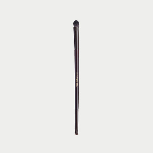 A single makeup brush with a dark brown handle and black bristles, featuring gold text that reads 'The Makeup Club' on a light gray background.