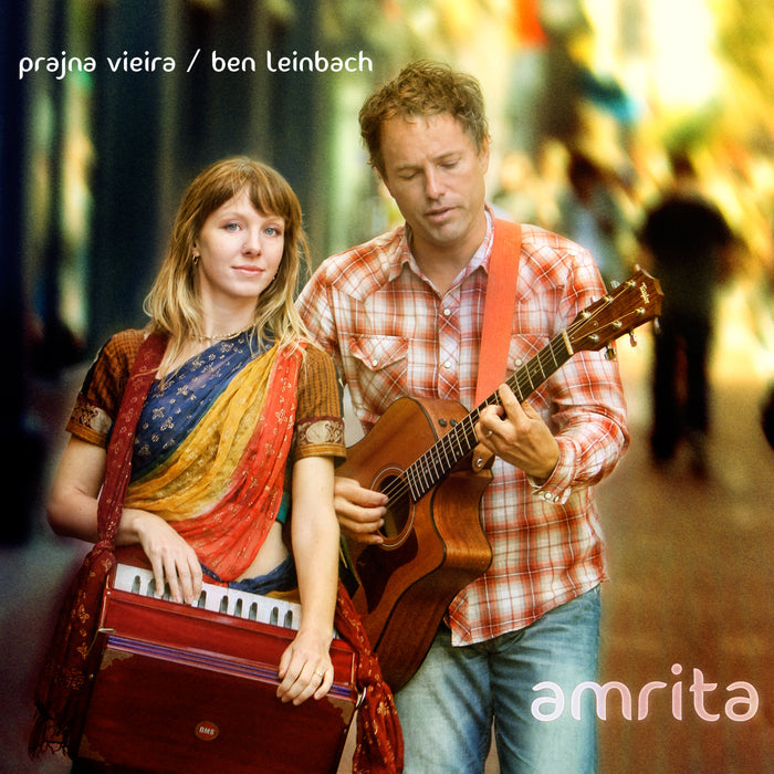 A woman in a vibrant sari plays harmonium beside a man in plaid playing acoustic guitar on a city street. Text: Prajna Vieira / Ben Leinbach and Amrita. Play sample audio for an exclusive preview.