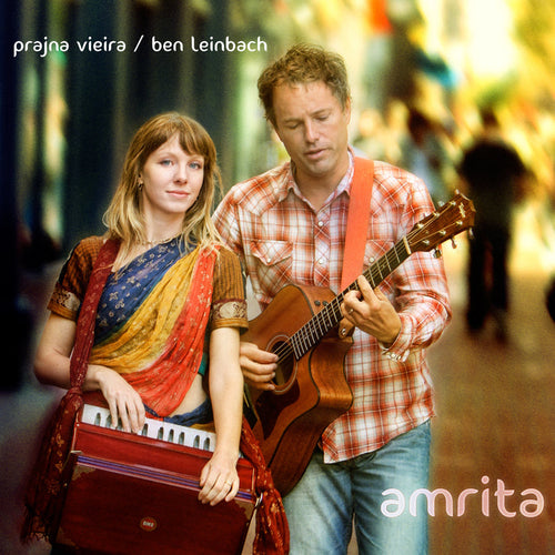 A woman in a vibrant sari plays harmonium beside a man in plaid playing acoustic guitar on a city street. Text: Prajna Vieira / Ben Leinbach and Amrita. Play sample audio for an exclusive preview.