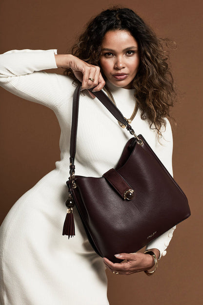 Female model holding the Andrea Black Cherry faux leather Hobo shoulder bag by the shoulder strap with her hands
