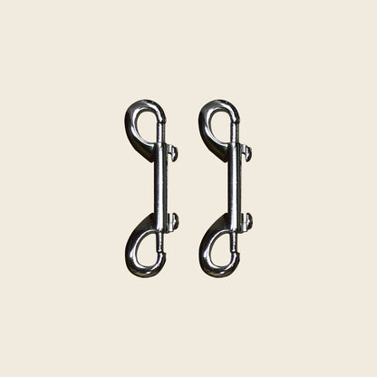 Pair of chrome double-ended snap hooks for Pilates Cadillac and reformer equipment.