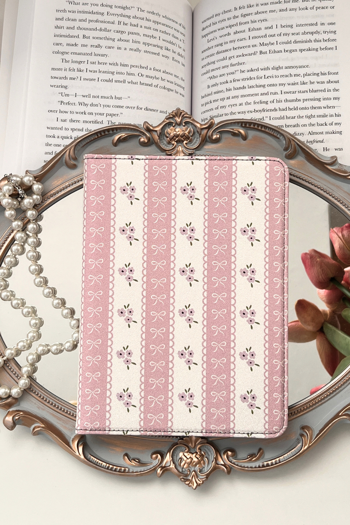 Pink patterned kindle on a decorative stand with a book and flowers in the background