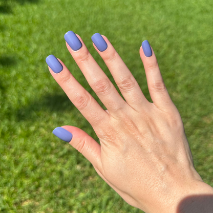 Hand displaying Bootcut | Short | Squoval - Tab Press-On nails in denim blue shade outdoors on green grass background