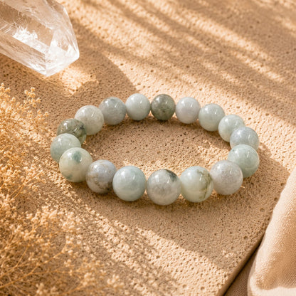 A beaded stretch bracelet made of Jade round beads, displayed on a textured beige fabric with warm sunlight and shadows.