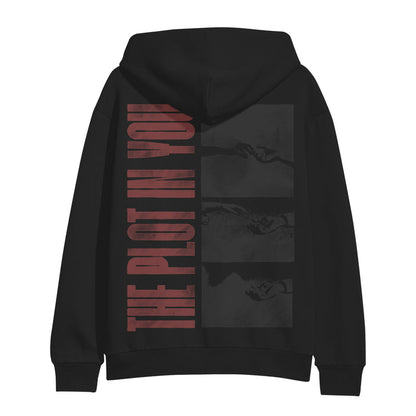 A black hoodie by The Plot In You, featuring bold red lettering down the back and three grayscale panels of hands reaching for each other.
