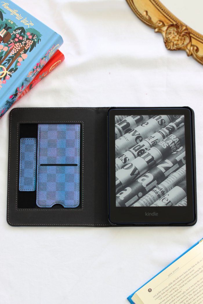 Two Kindle devices in a black leather case on a white surface with books and a pen.