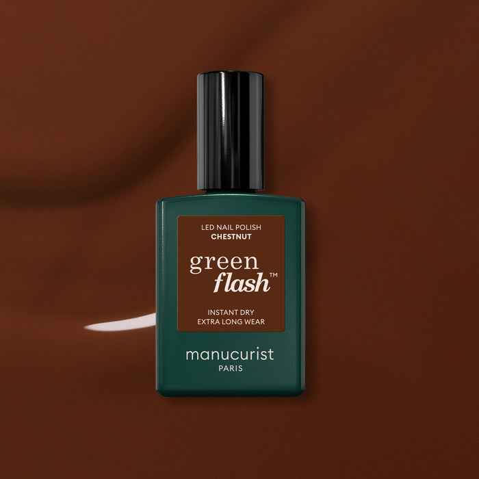 A green Manucurist bottle of Green Flash™ gel polish in Chestnut, a warm brown shade, is set against a glossy brown background.