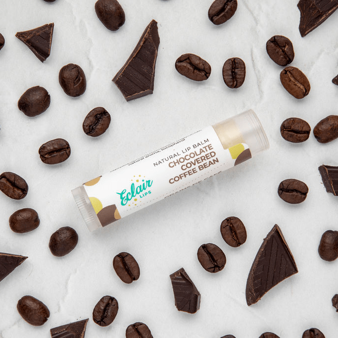 Chocolate-covered coffee bean lip balm surrounded by coffee beans and chocolate