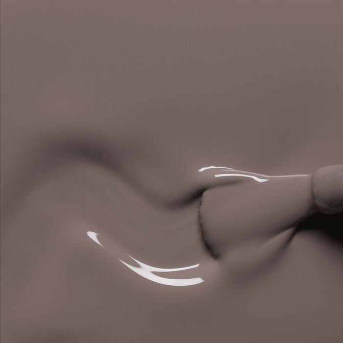 A close-up of a Manucurist Clay nail polish brush gliding smooth, glossy taupe gel onto a surface, forming gentle swirls with reflective highlights.
