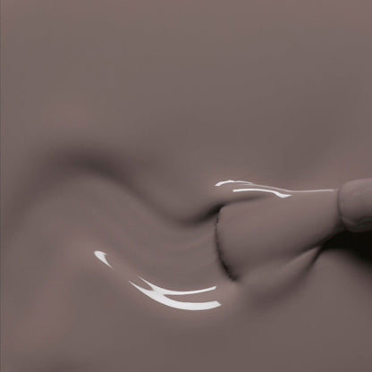 A close-up of a Manucurist Clay nail polish brush gliding smooth, glossy taupe gel onto a surface, forming gentle swirls with reflective highlights.