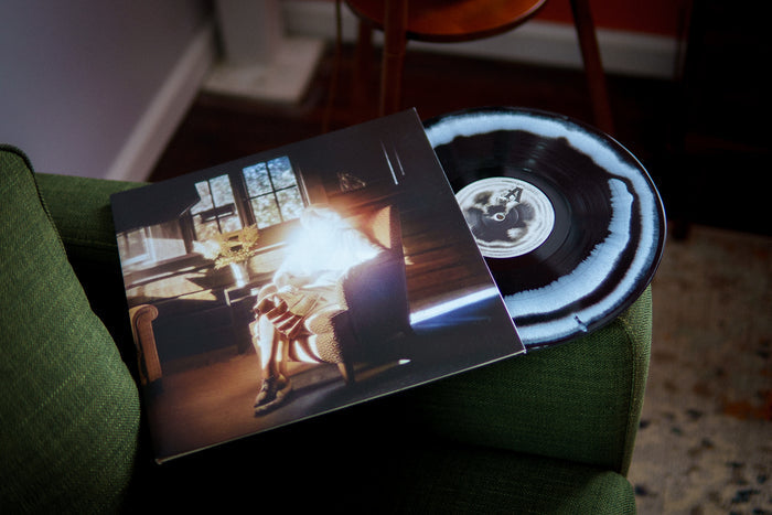 A Black with White marbled Common Sage vinyl and sleeve, featuring a person by a sunlit window in a cozy wooden room, rest on a green sofa in warm light. Brand: Common Sage. Ships via USPS Priority Mail.