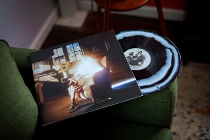 A Black with White marbled Common Sage vinyl and sleeve, featuring a person by a sunlit window in a cozy wooden room, rest on a green sofa in warm light. Brand: Common Sage. Ships via USPS Priority Mail.