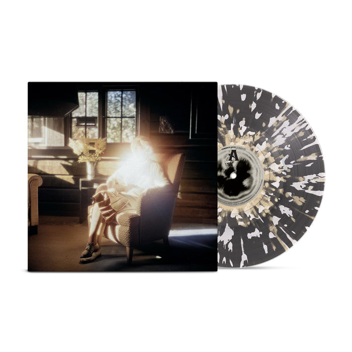 A transparent black vinyl with bone and white splatter peeks out of a jacket which shows a glowing, backlit figure in an armchair by a window in a sunlit rustic room.