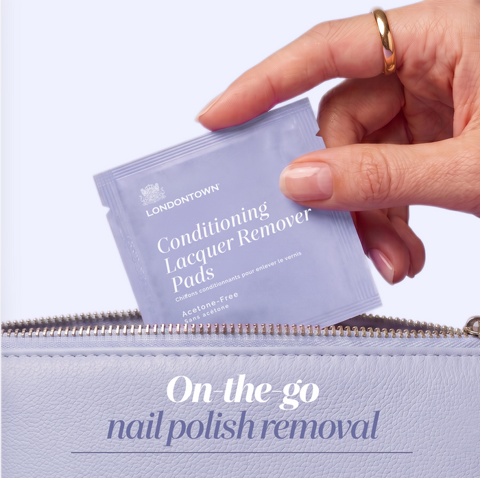 A hand places a packet of LONDONTOWN Conditioning Lacquer Remover Pads into a light purple zippered pouch. Text below reads, "On-the-go nail polish removal.