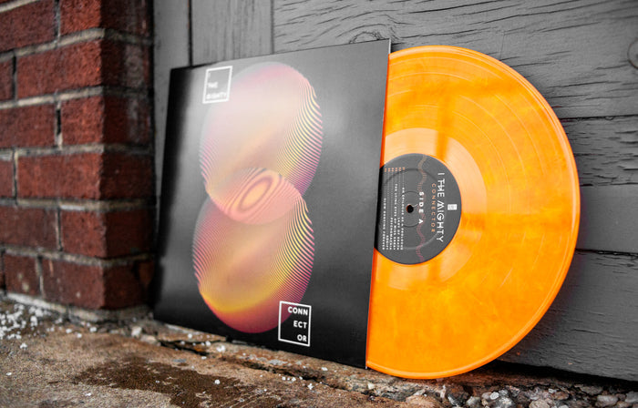An orange/yellow marble vinyl peeks out of a black cover with two orange and red fingerprint designs overlapping one another. In white words, " I The Mighty" is at the top of the cover and "Connector" is at the bottom. The cover rests on a black door next to a brick wall outside.