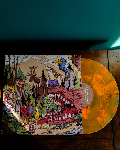 A Lot Like Birds’ Limited Edition orange marbled vinyl sits partly in its illustrated sleeve—showing people and fantastical creatures at a forest Koi Pond—on a wooden surface under bright light.