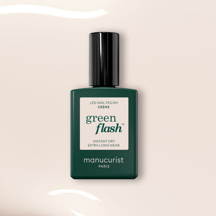 A bottle of Manucurist Crème gel polish in a dark green rectangular bottle with a black cap, standing upright on a light beige background with white light reflections.