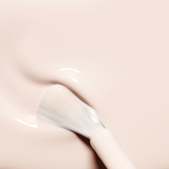 A brush applies Manucurist Crème, a milky pale pink gel nail polish, onto nails for a smooth, glossy finish with subtle swirls and a reflective sheen.