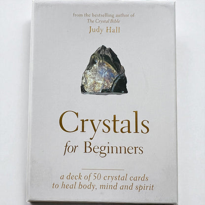 Card deck packaging titled 'Crystals for Beginners' by Judy Hall on a white background, Raven's Cauldron, 6 N Sandusky St, Delaware, OH 43015