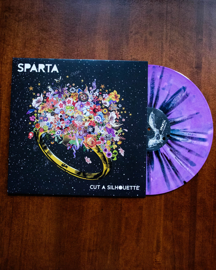 A limited edition Sparta vinyl record titled "Cut a Silhouette" features a vibrant floral ring on the cover and an eye-catching lilac vinyl, partially pulled out, displayed on a wooden surface.