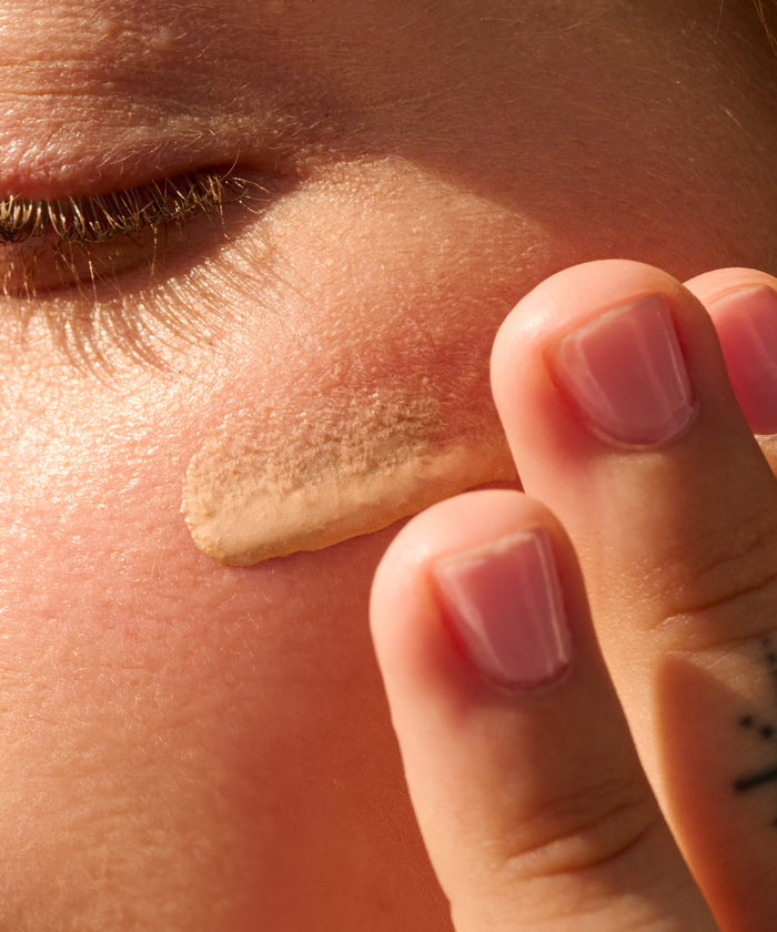 Close-up of a person applying Daily 30 Glow sunscreen by Sun Bum on their cheek near the eye.