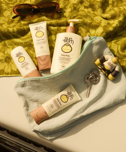 Sun Bum Daily 50 Body Lotion with other Sun Bum products arranged on a green towel and light fabric pouch outdoors.