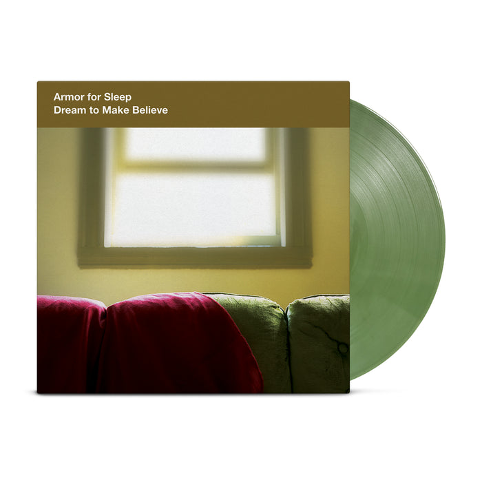 A translucent green shimmer vinyl record by Armor For Sleep partially slides out of its cover, featuring a soft-focus photo of a couch with a red blanket and sunlit window. The album is Dream To Make Believe.