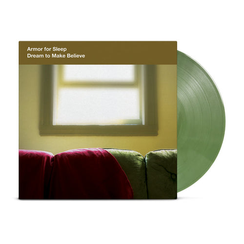 A translucent green shimmer vinyl record by Armor For Sleep partially slides out of its cover, featuring a soft-focus photo of a couch with a red blanket and sunlit window. The album is Dream To Make Believe.