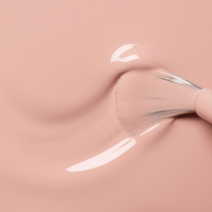 A brush applies Manucurist's Dune, a smooth, glossy light pink polish, on a matching surface, creating an even stroke—perfect for pairing with beige gel accents.