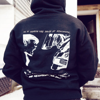 On the back, there is a drawing of a boy yelling in the face of a police officer that is much taller than him. Below that drawing is more text that is stacked in gradient coloring, getting more visible toward the bottom of the hoodie. An individual is modeling the hoodie, standing in front of two buildings. There is snow on the ground.