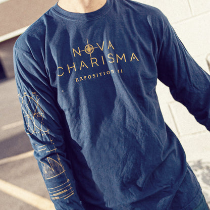 Navy long sleeve shirt with NOVA CHARISMA written across the chest. Inside the letter O of NOVA, there is a starlight design coming out of it. Below NOVA CHARISMA, there is smaller text that says EXPOSITION III. On one of the sleeves, there are various designs of graphs and data. An individual is modeling the shirt and standing in front of a building and in a parking lot.