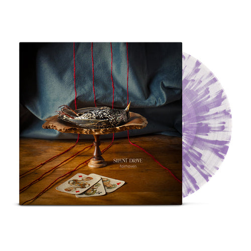 A Silent Drive Fairhaven Vinyl LP is displayed in white and clear/lilac splatter. The cover shows a dead bird on a silver dish, red strings above, and two playing cards. Album: Fairhaven by Silent Drive.