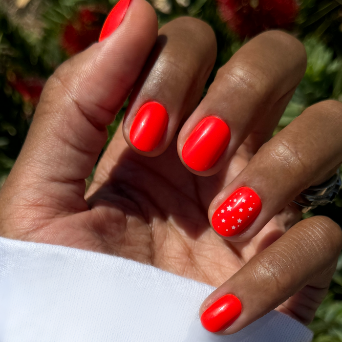 Festive Stars | Extra Short | Round - Tab Press-On nails in bright red with small white star details on natural hand outdoors