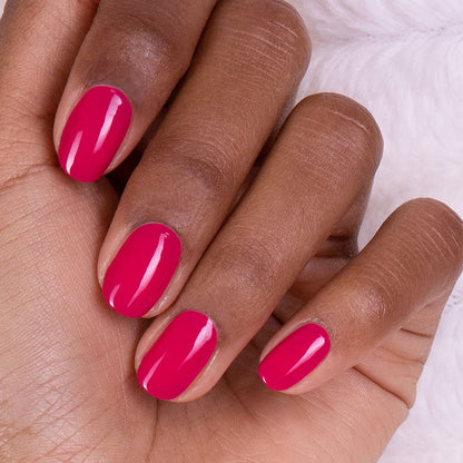 A hand with medium-dark skin tone shows neatly manicured nails painted in glossy "Fuchsia" gel polish by Manucurist, set against a soft white background.