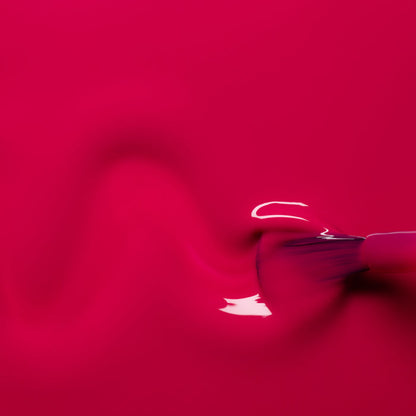 A close-up of a brush spreading Manucurist Fuchsia gel polish in a wavy line on a smooth surface, with glossy reflections highlighting the vibrant pink color.