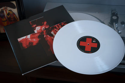 An opaque white vinyl marked with a red cross sits partially out of its black album cover, which shows a red cross and blurred concert photo, on a turntable. Limited to 800 copies, its the Bane Give Blood Deluxe Edition.
