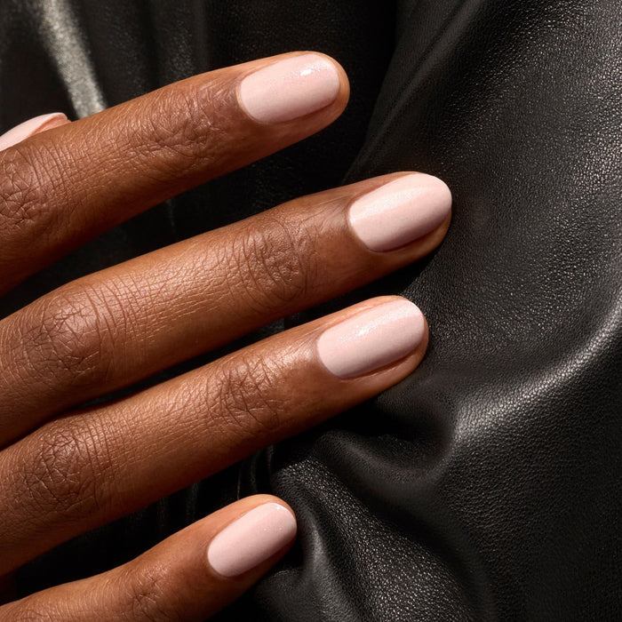 A close-up of a hand with neatly manicured nails painted in Manucurist Gloss, a glossy pink nail polish, resting on a black leather surface.
