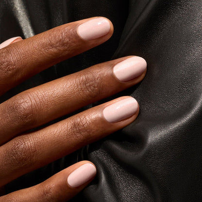 A close-up of a hand with neatly manicured nails painted in Manucurist Gloss, a glossy pink nail polish, resting on a black leather surface.